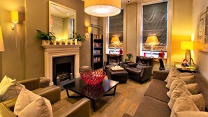A well-lit living room with a fireplace, leather sofas, a coffee table, and a bookshelf. - The Sumner (London)