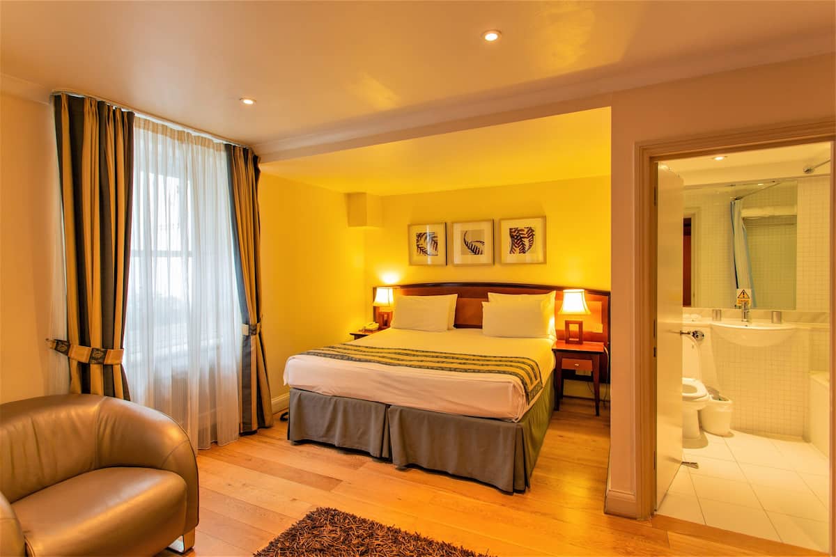Ein Hotelzimmer mit Bett, Stuhl, Nachttisch und einem durch eine offene Tür einsehbaren Badezimmer.