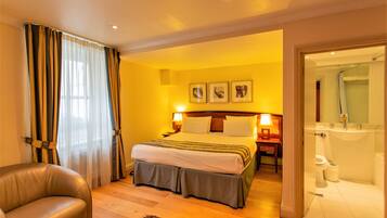 A hotel room with a bed, a chair, a nightstand, and a bathroom visible through an open door.