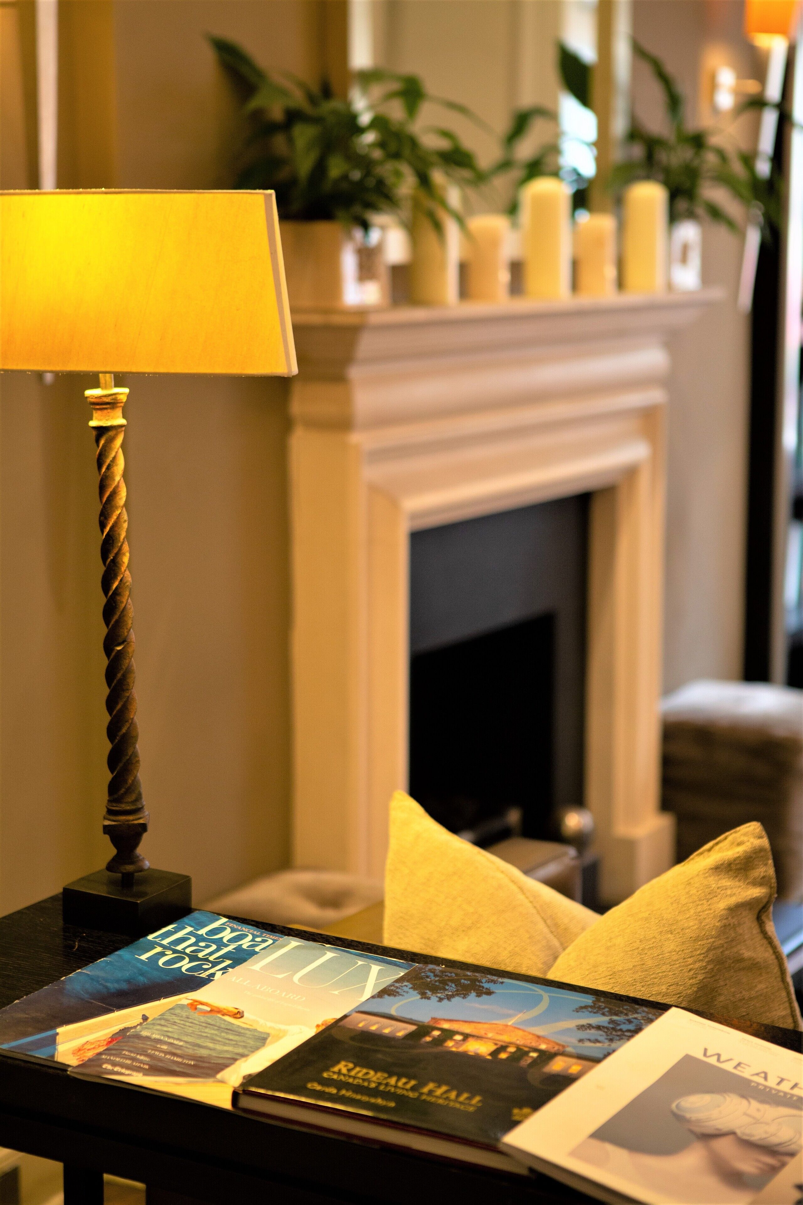 A room with a fireplace, a lamp, and a table with magazines.