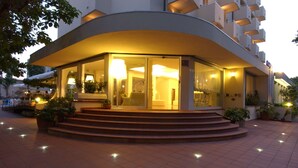 A modern hotel with a curved facade, glass entrance, and outdoor seating area. - Hotel Sport & Residenza (Cesenatico)
