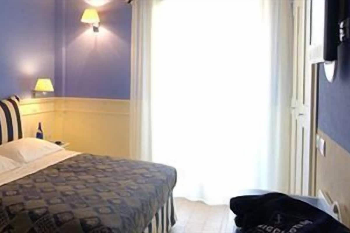 A hotel room with a bed, a nightstand, a lamp, and a door.