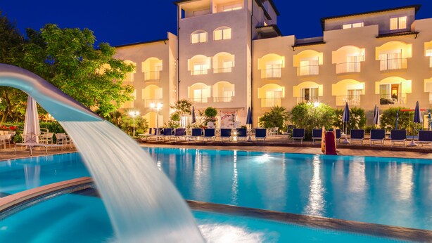 A swimming pool with a water slide, lounge chairs, and a building with multiple balconies in the background. - Hotel Sport & Residenza (Cesenatico)