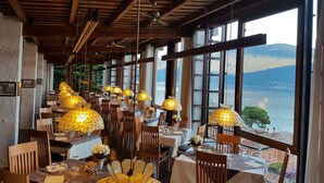 A restaurant with wooden beams, large windows, and table lamps. - Palazzina (Gargnano)