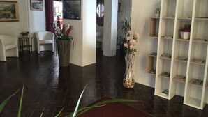A spacious living area with a dark wooden floor, white walls, and a red carpet. There are white shelves with books and decorative items, a white armchair, and a table with a vase of flowers. - Palazzina (Gargnano)