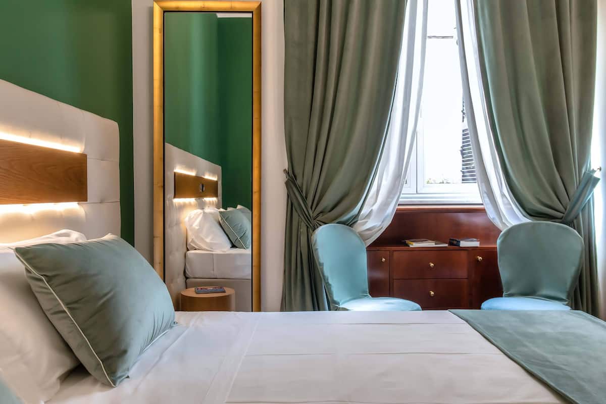 Una habitación de hotel con una cama, dos sillones, una mesita de noche de madera y un aparador.