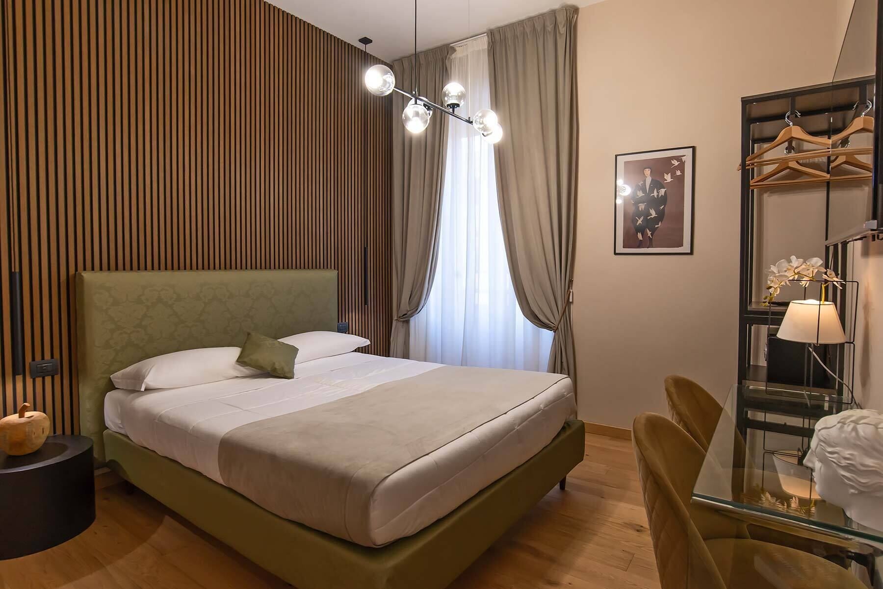 A modern hotel room with a large bed, a bedside table, a chair, a wardrobe with a mirror, and a hanging light fixture.