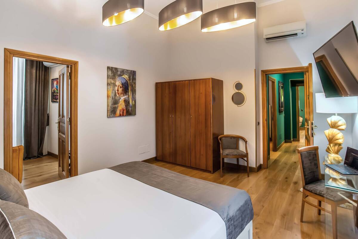 Un dormitorio con cama, armario de madera y escritorio con silla. Hay un cuadro en la pared y un equipo de aire acondicionado.