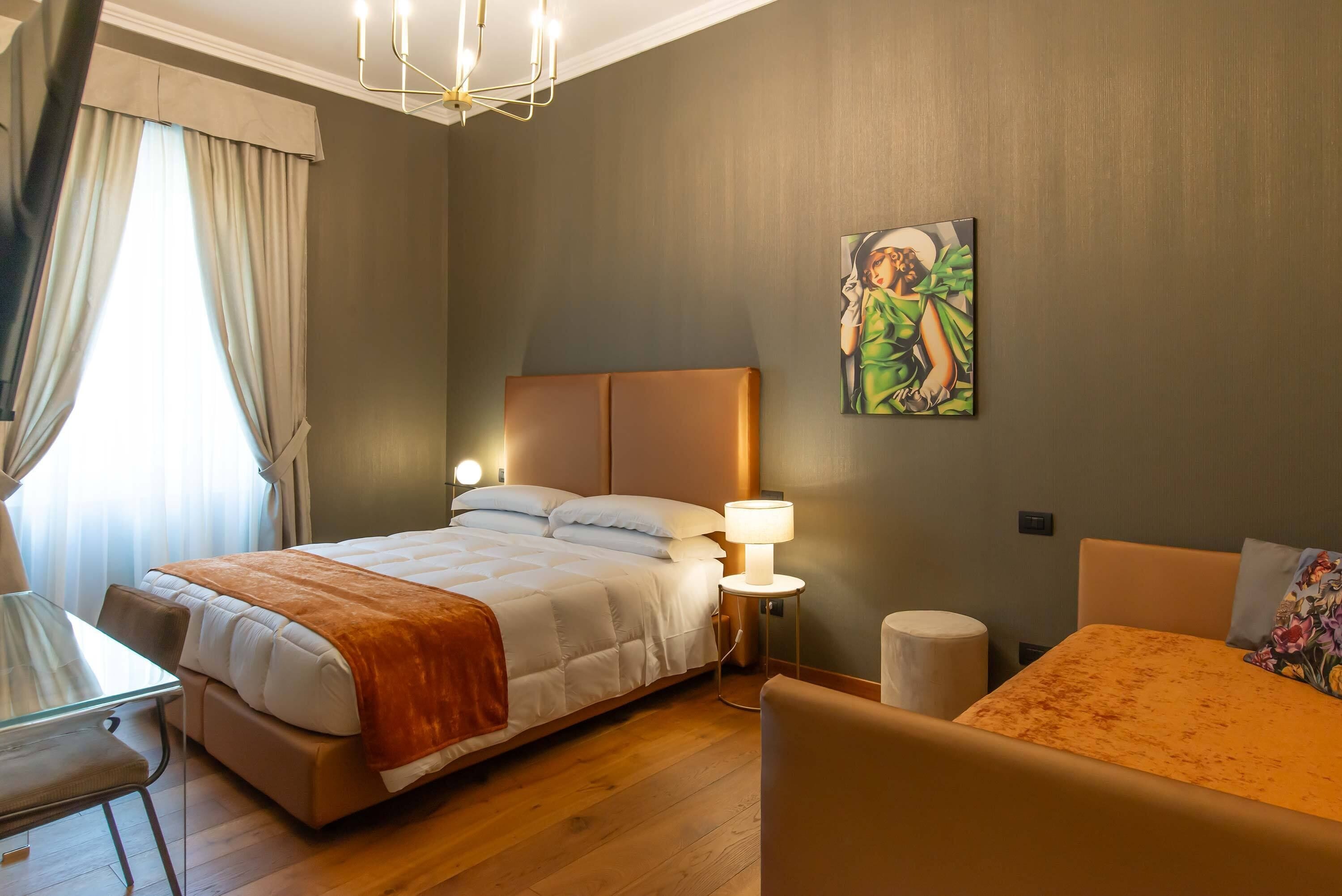 A bedroom with a bed, bedside table, lamp, and a painting on the wall.