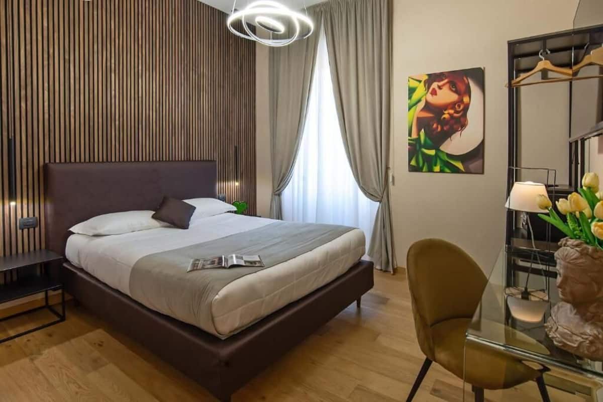 Habitación de hotel moderna con una cama grande, un escritorio con silla, un cuadro en la pared y un florero con flores.