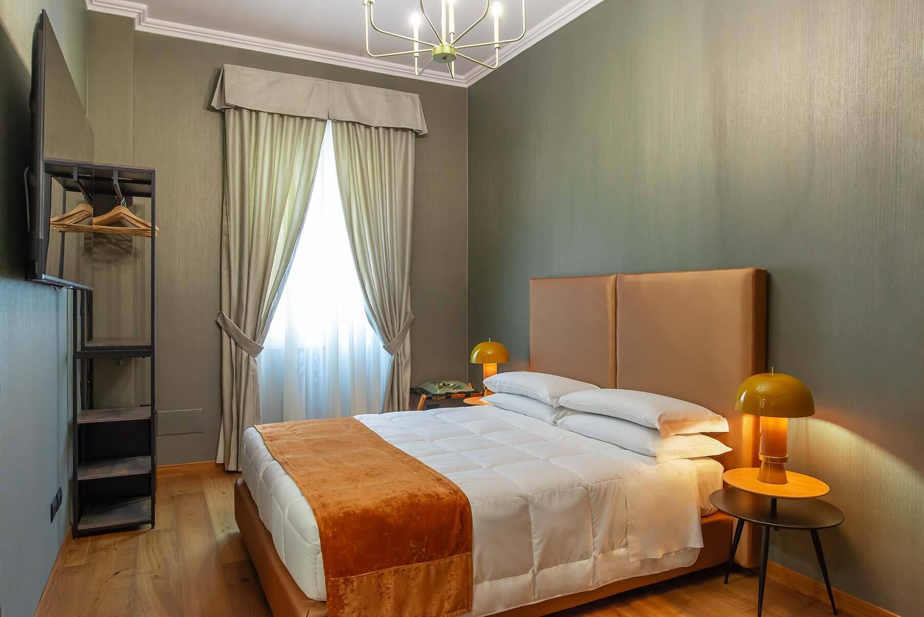 A hotel room with a bed, bedside lamps, a wardrobe, and a window with curtains.