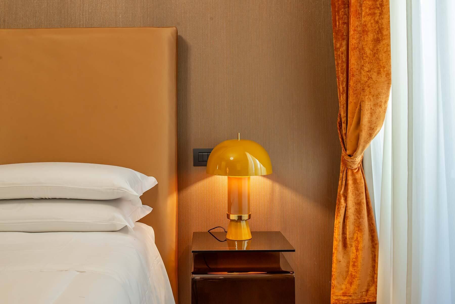 A hotel room with a bed, a nightstand with a lamp, and a window with curtains.