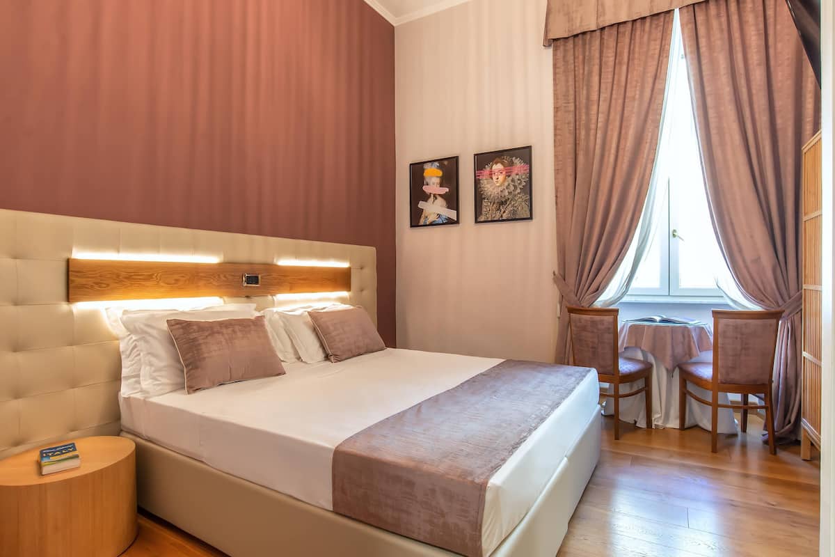 Una cama bien hecha con cabecera, mesita de noche y ventana con cortinas.