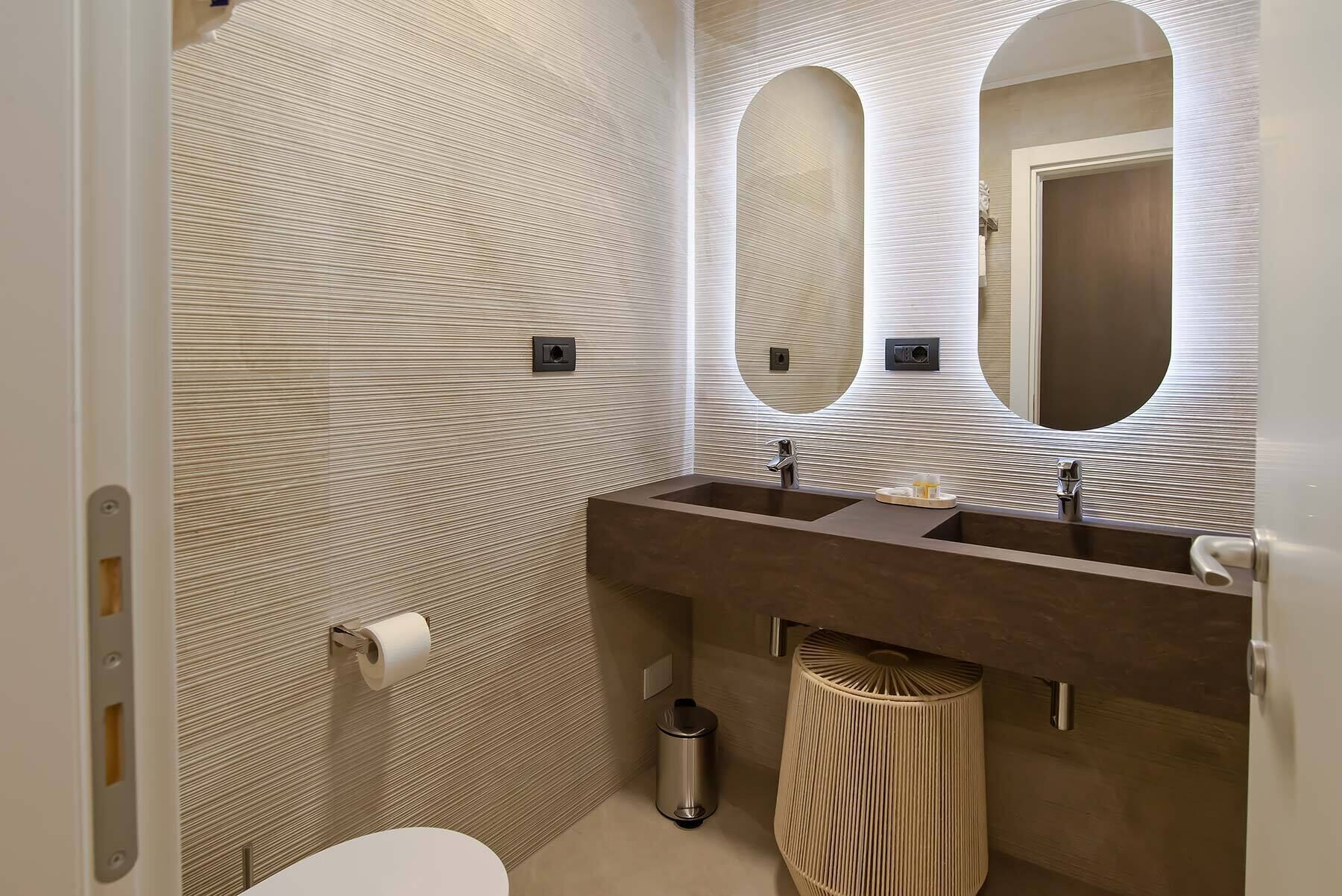 Ein modernes Badezimmer mit einem großen Spiegel, zwei Waschbecken und einer Toilette.