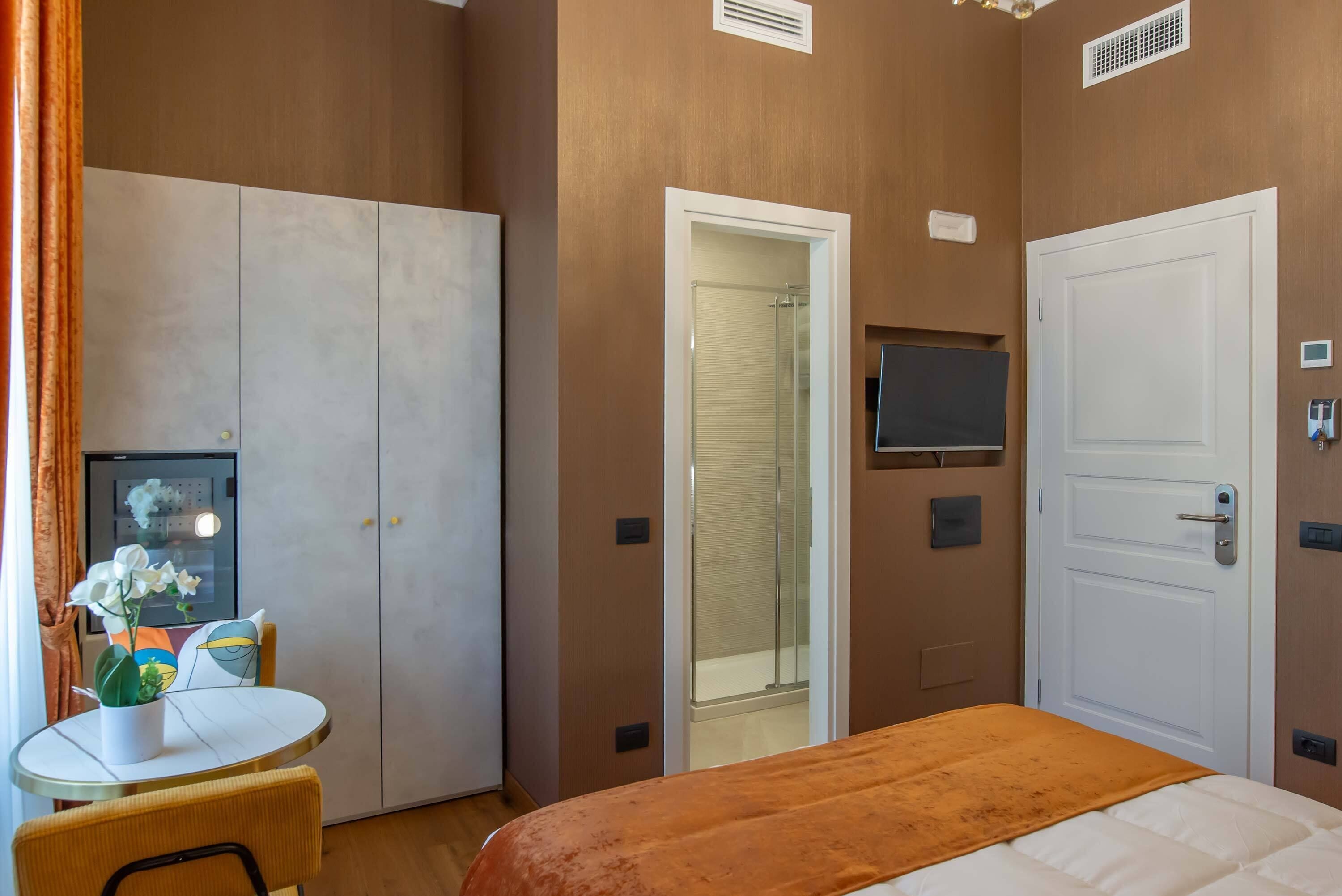 Ein Hotelzimmer mit einem Bett, einem Fernseher, einem Kleiderschrank, einer Tür und einem kleinen Tisch mit Blumen in einer Vase.