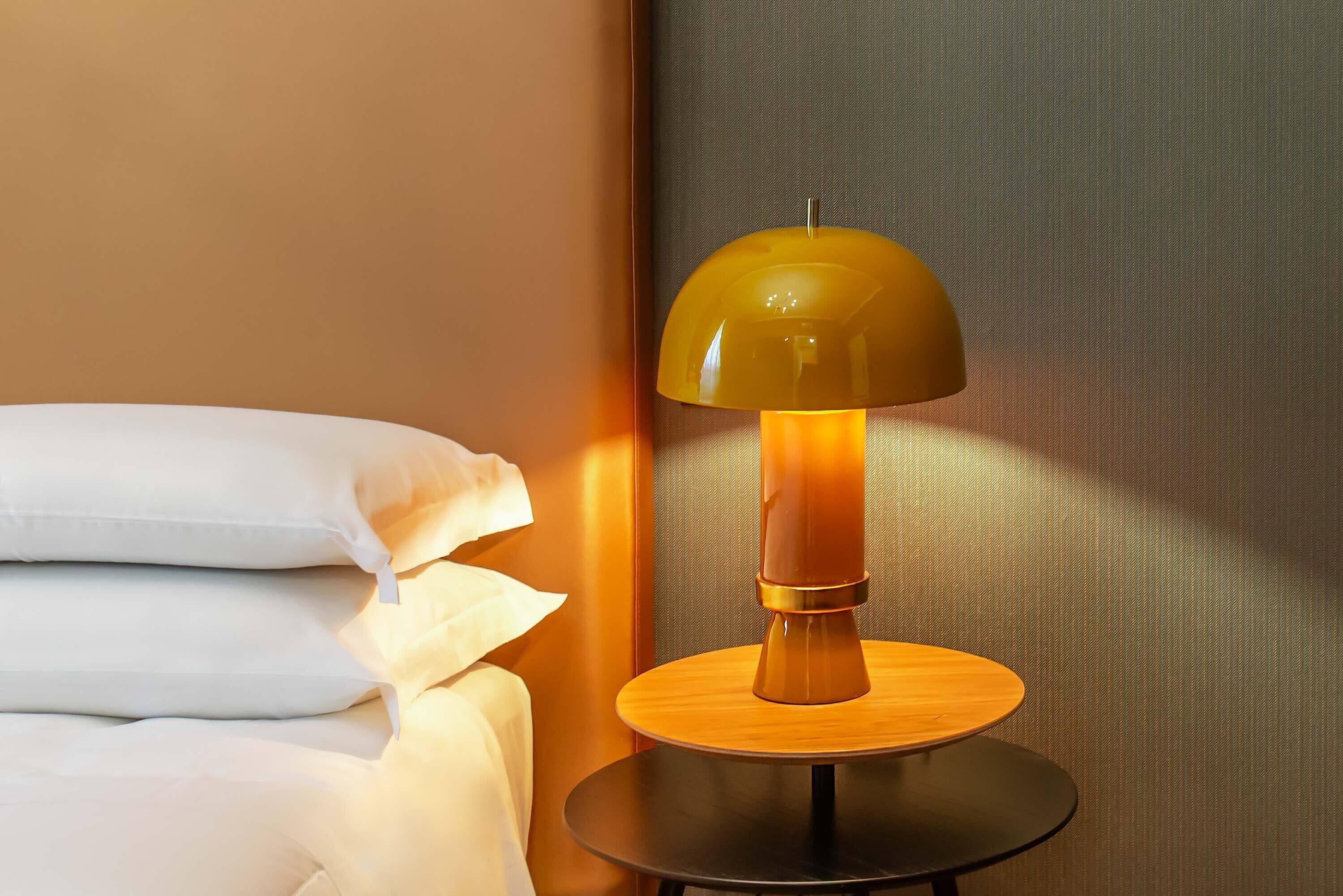 A bed with white bedding and a round table with a lamp.
