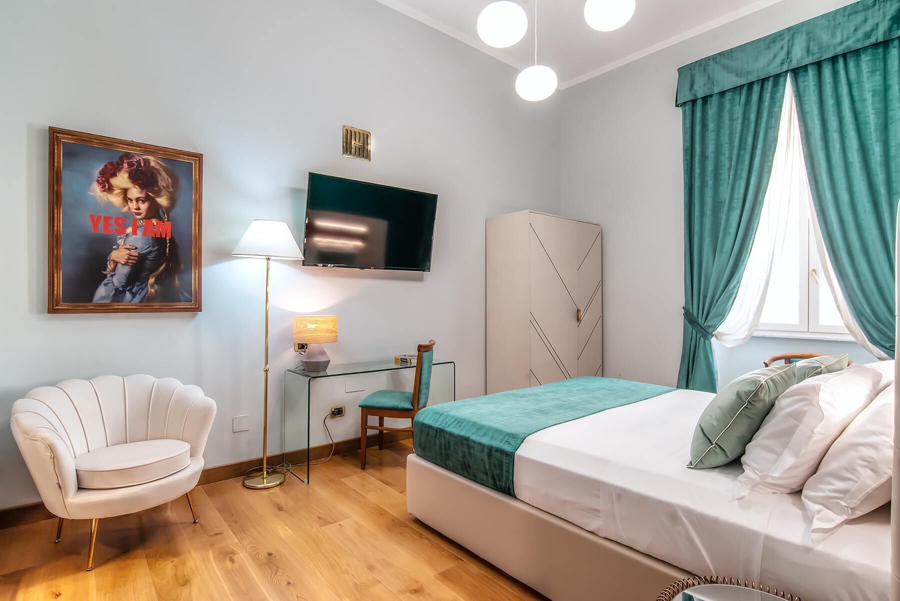 A bedroom with a bed, a chair, a desk, a TV, and a wardrobe.