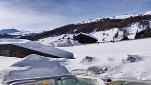 Un bain à remous avec des canards en plastique, entouré d’un paysage enneigé et de montagnes.
