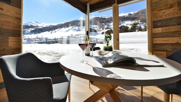 Un coin repas moderne avec une table ronde, deux chaises, une bouteille de vin et un magazine.