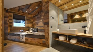 Une chambre moderne avec un mur décoré en bois, une grande fenêtre, un lit avec des oreillers et une étagère intégrée en bois où sont rangées des serviettes.