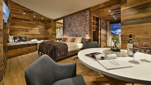 Une chambre d’hôtel moderne avec un décor intérieur en bois, un lit offrant une belle vue, une table à manger avec un magazine et des verres à vin, et un coin salon confortable.
