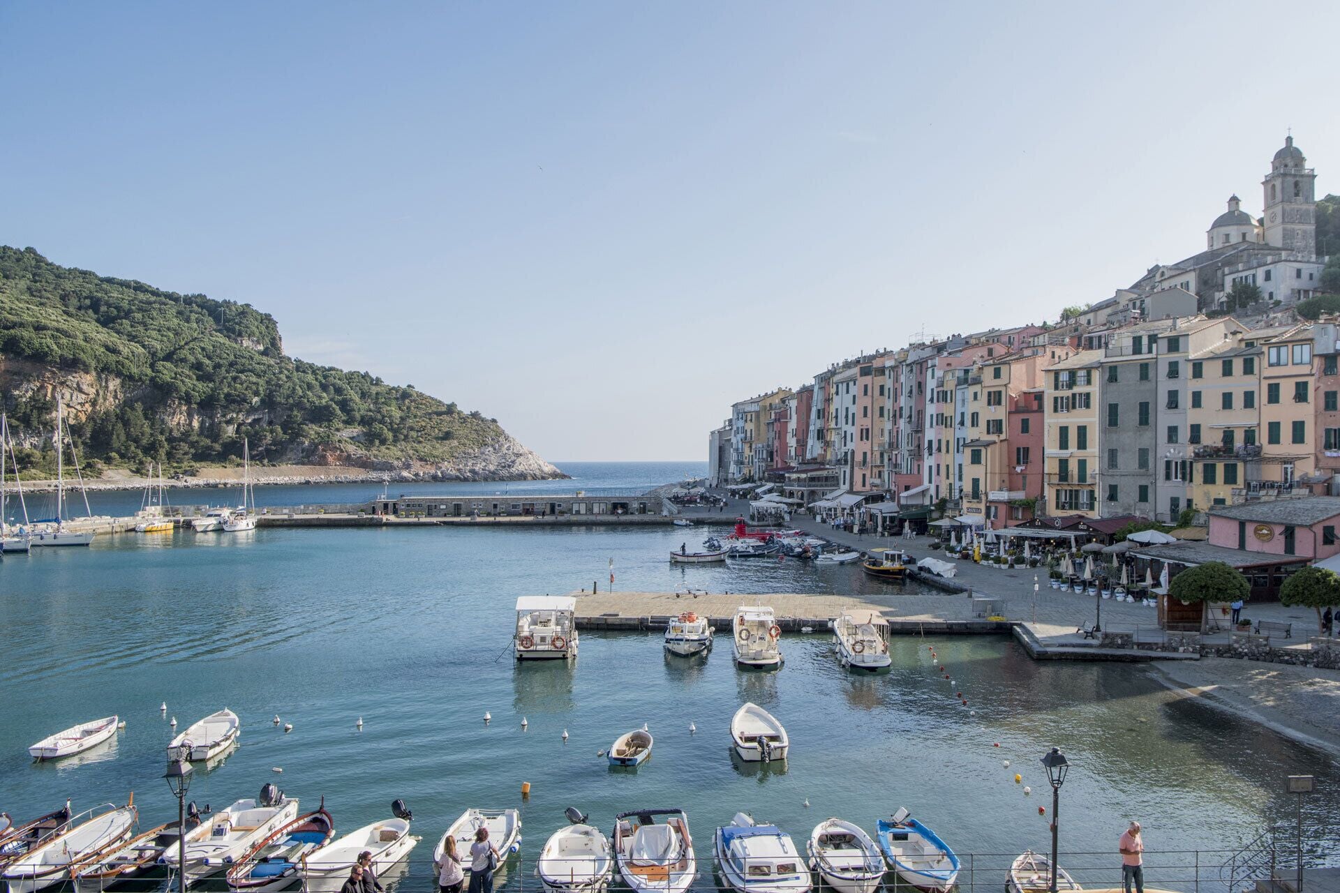 A coastal town with colorful buildings, a marina with boats, and a hilly backdrop.