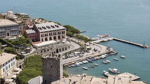 Un pueblo costero con edificios históricos, un puerto deportivo con barcos y una imponente estructura que parece un castillo.