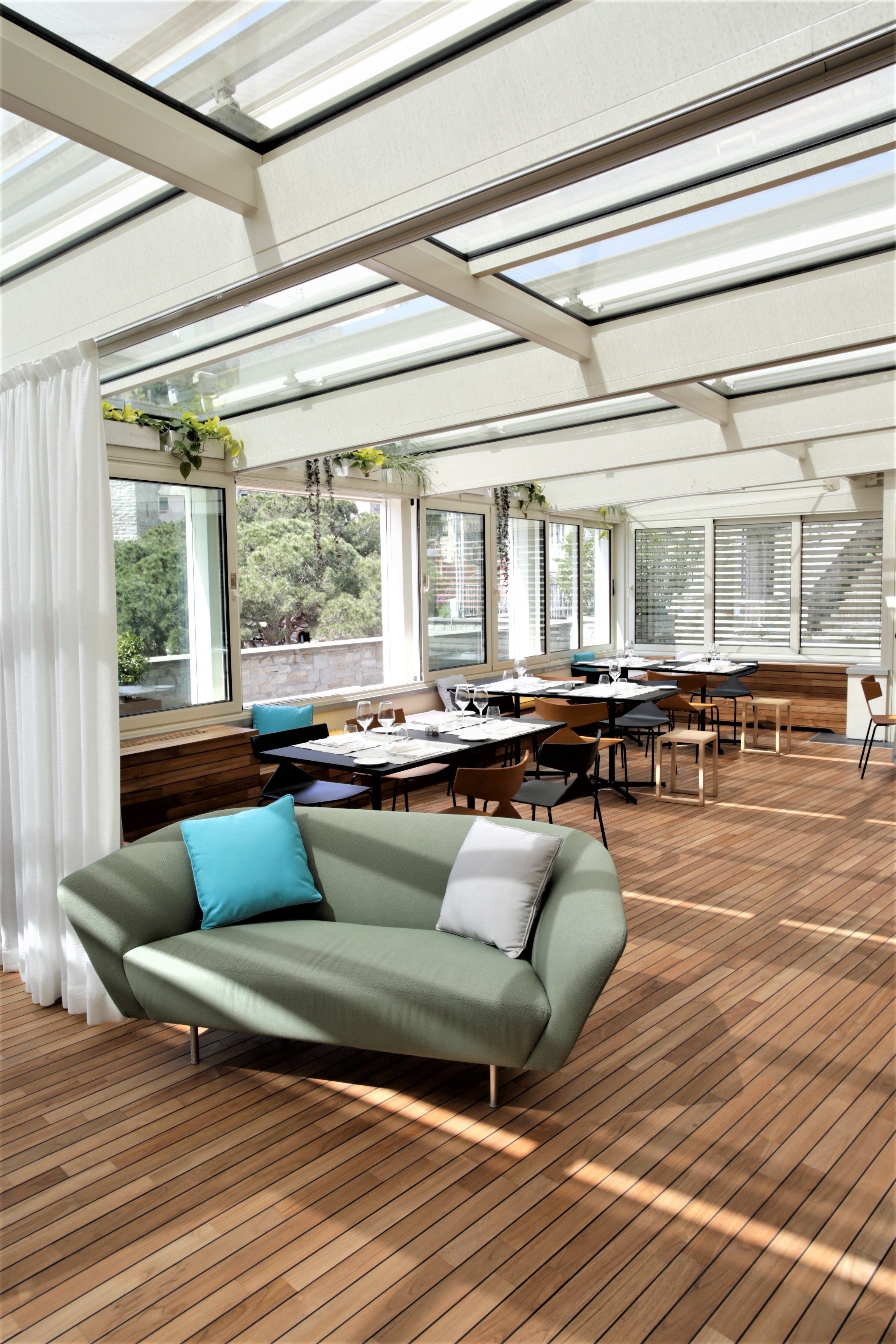 A modern interior with a wooden floor, a green sofa with blue cushions, and a dining area with tables and chairs.
