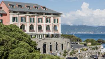 A large hotel with multiple stories, a prominent arched entrance, and a view of the sea.
