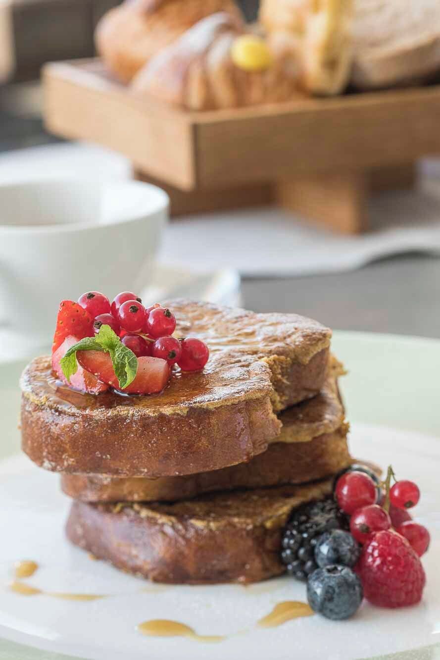 A stack of French toast with berries and syrup on a plate.