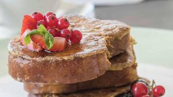 Una pila de tostadas francesas con bayas y jarabe sobre un plato.