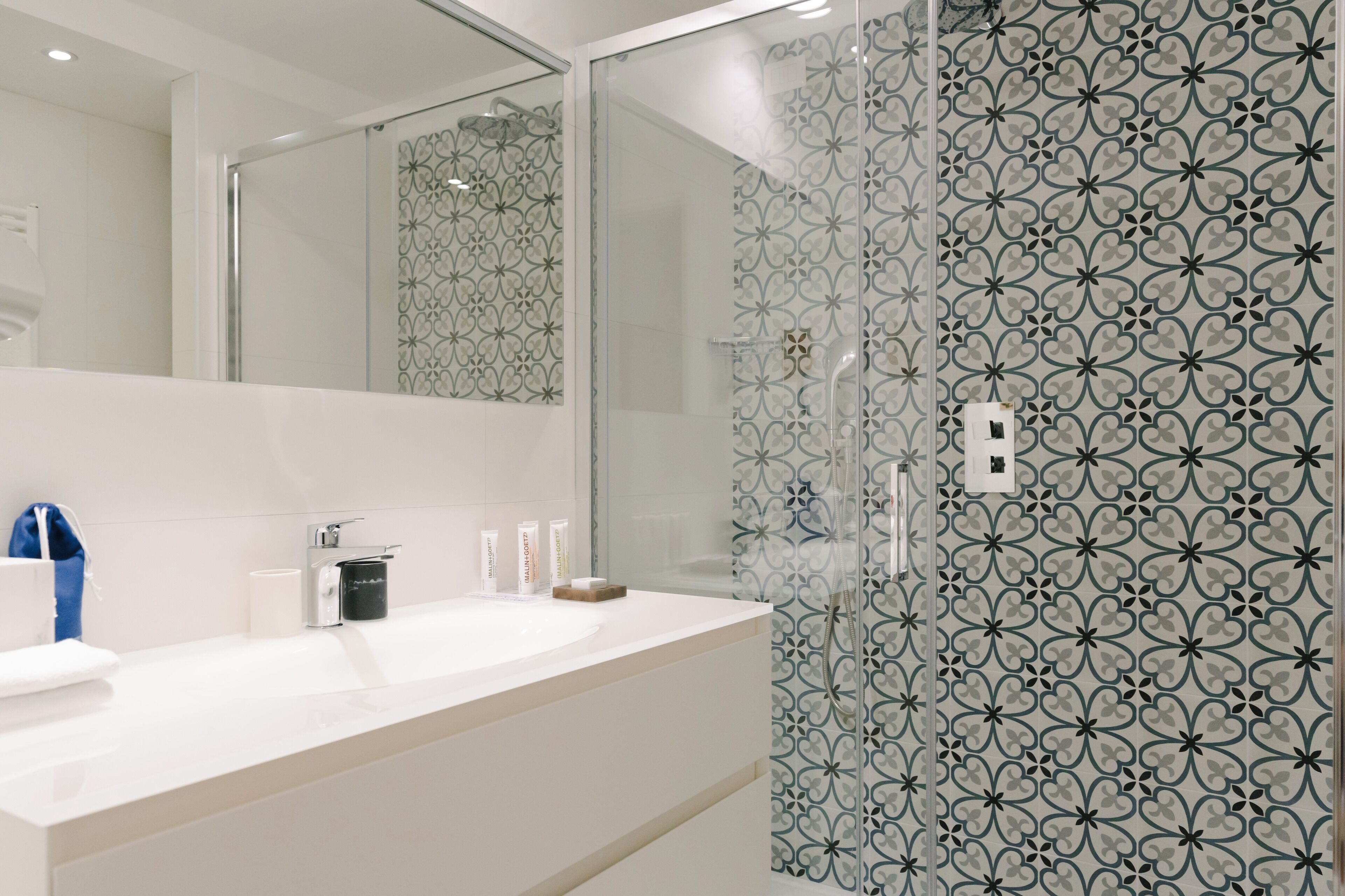 A modern bathroom with a white sink, mirror, and patterned glass shower enclosure.