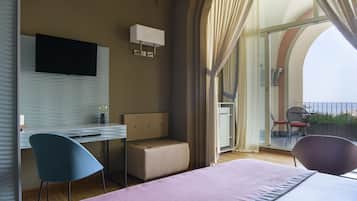 Quarto de hotel moderno com cama, escrivaninha, cadeira, televisão e varanda com cadeira e plantas.