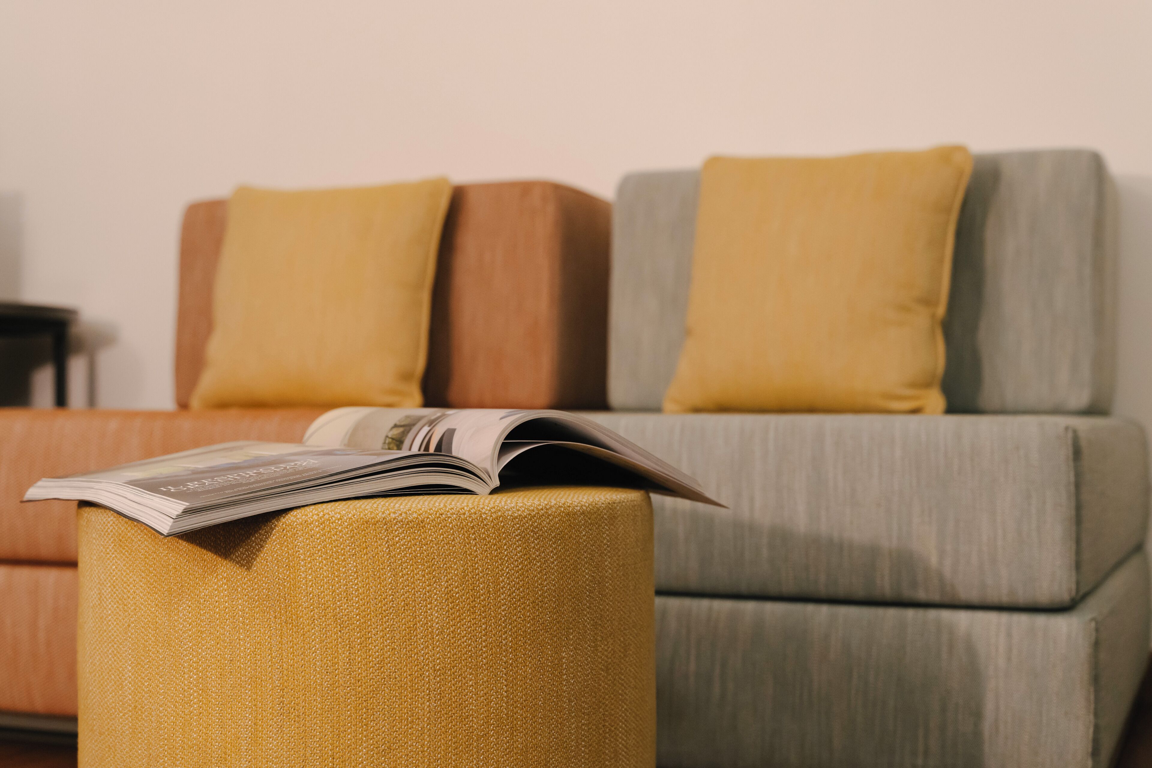 Ein modernes Wohnzimmer mit Sofa und Hocker, auf dem ein Magazin liegt.
