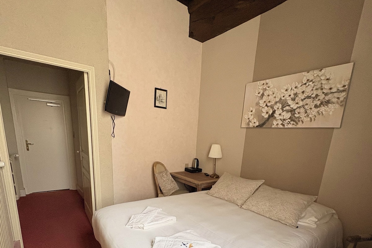 Una habitación de hotel con una cama, una mesita de noche, una silla, un cuadro en la pared y una puerta que da a otra habitación.