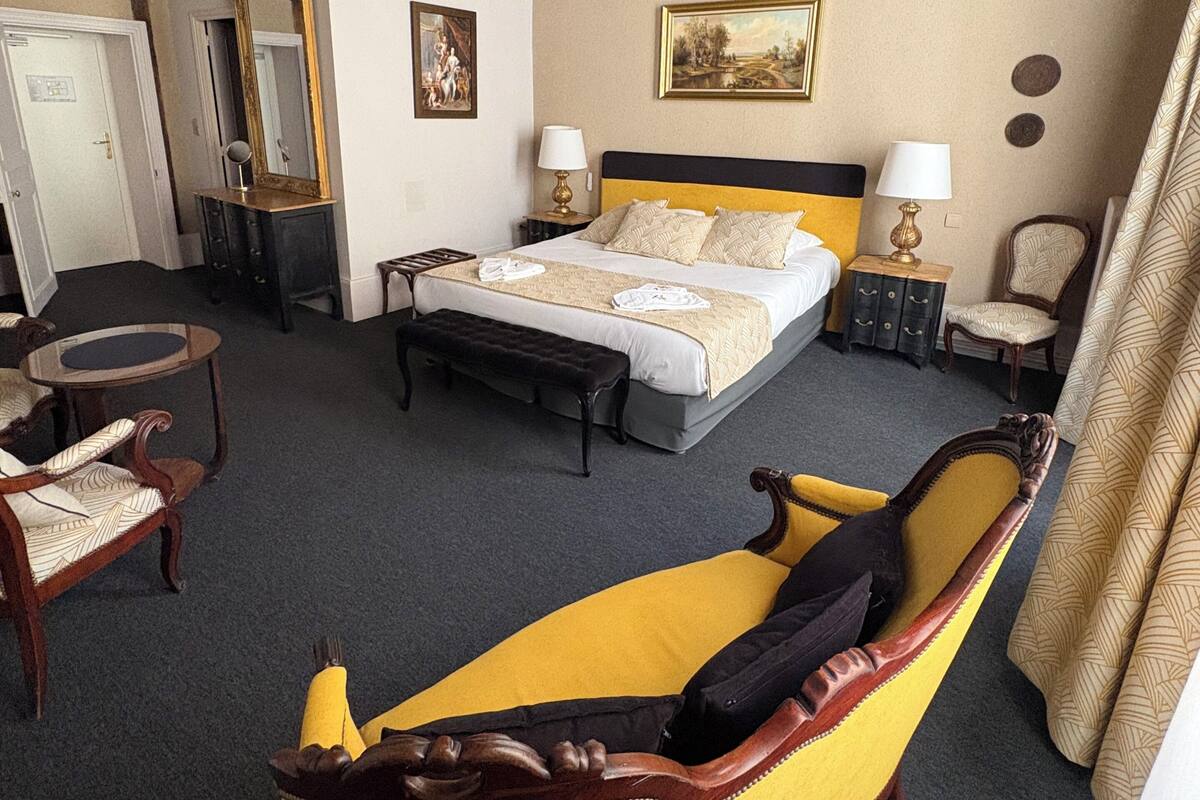 Habitación de hotel con una cama, un banco, una silla, un escritorio, un espejo y un cuadro en la pared.