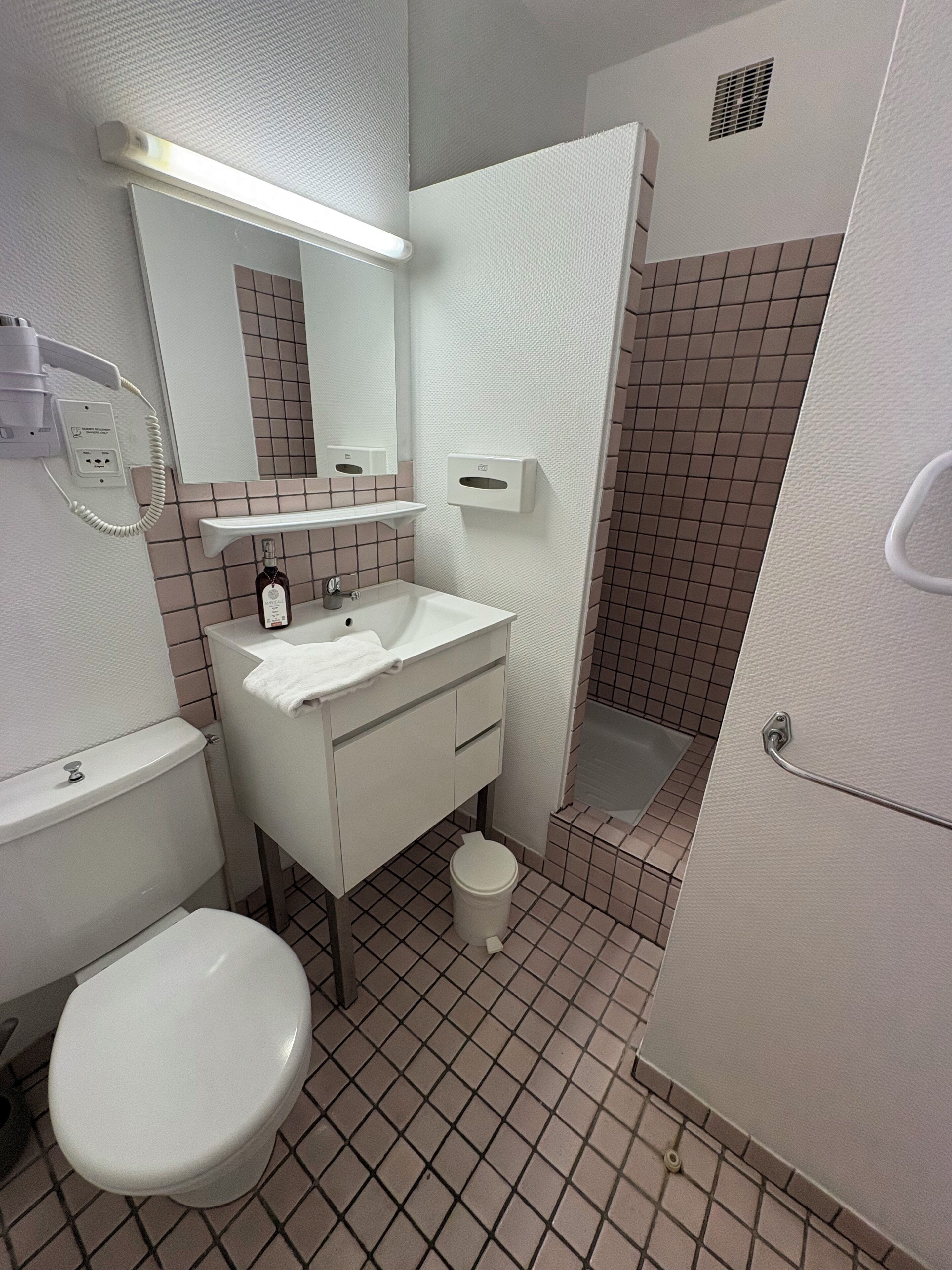 A bathroom with a toilet, sink, mirror, and shower.