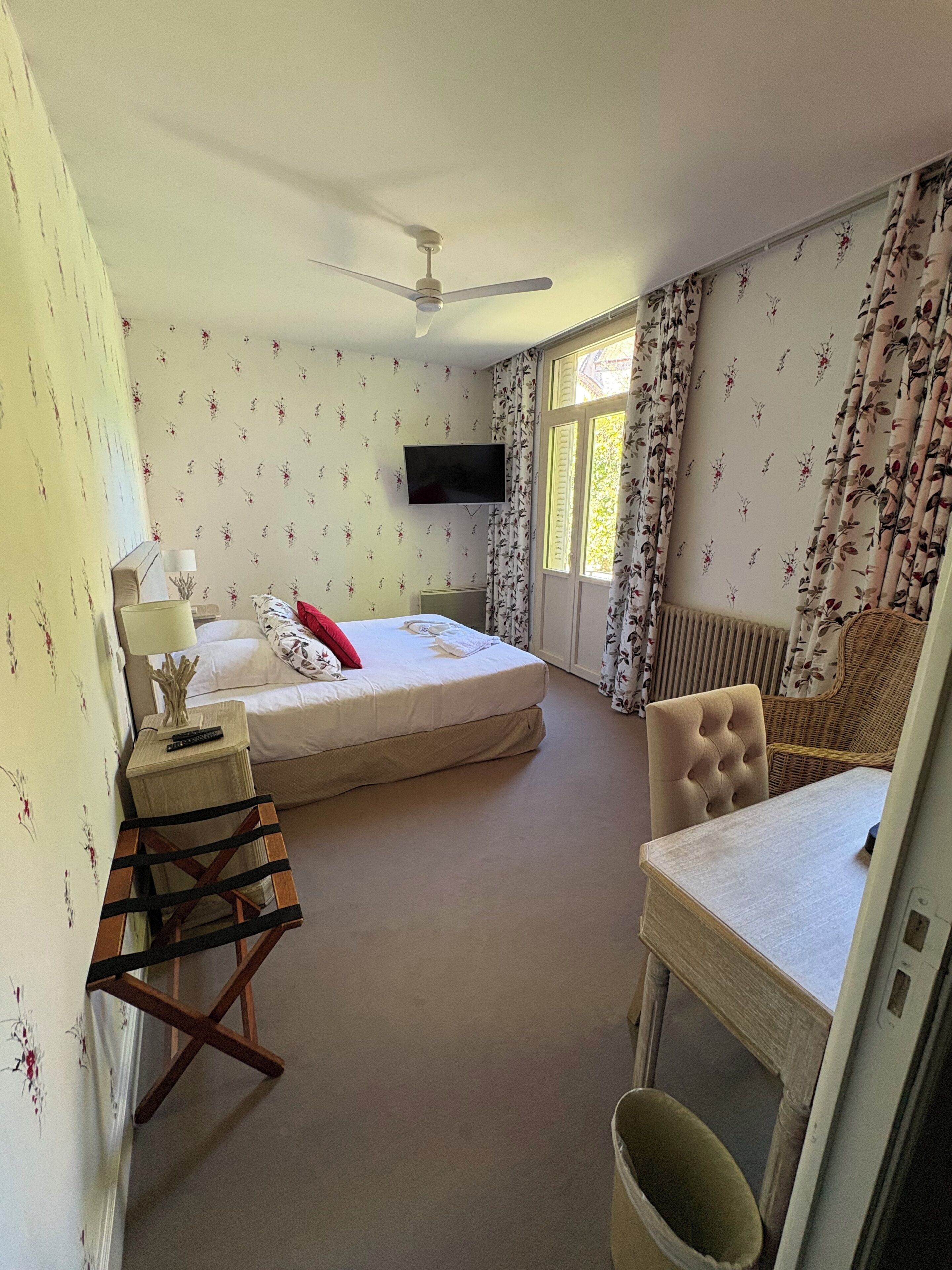 A bedroom with a bed, a television, a chair, a table, and a window with curtains.
