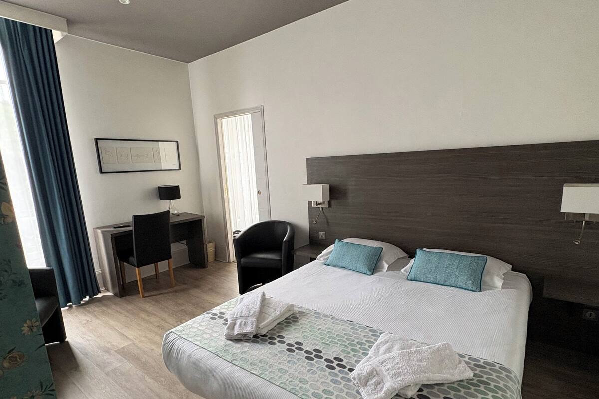 Una habitación de hotel moderna con una cama grande, un escritorio, una silla y un ventanal con cortinas.