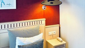 Una habitación con una cama, una mesita de noche con un teléfono y una lámpara de pared.