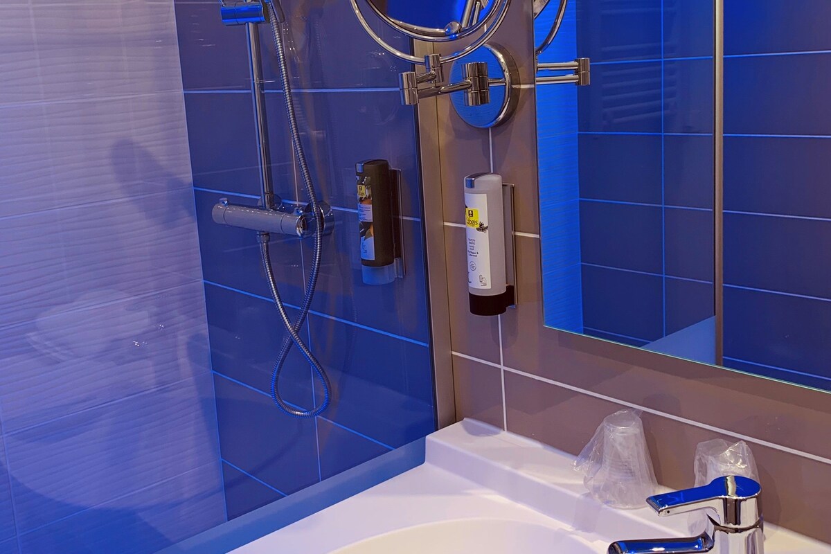 Un baño moderno con un lavamanos blanco, un cabezal de ducha de mano, un espejo montado en la pared y un cabezal de ducha de mano.