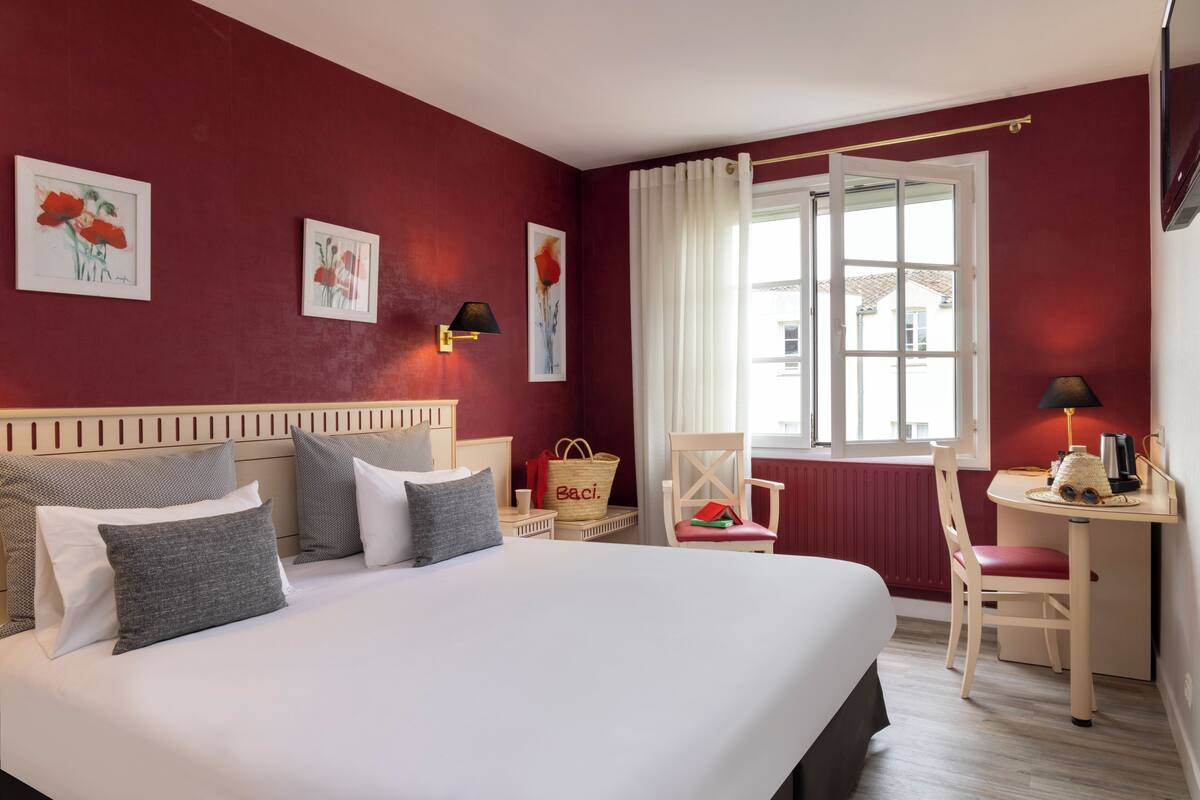 Quarto de hotel com cama, escrivaninha, cadeira e obras de arte nas paredes.
