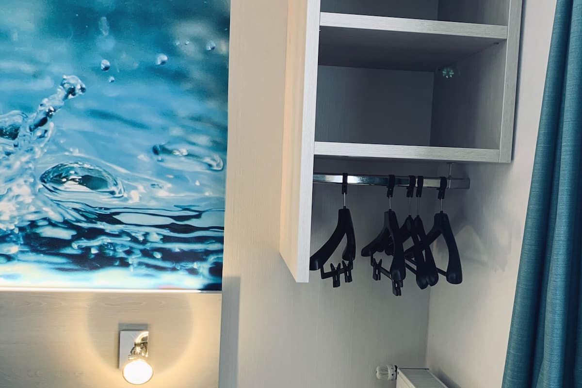 A small room with a bed, a wall-mounted shelf, a radiator, and a wall art depicting water.