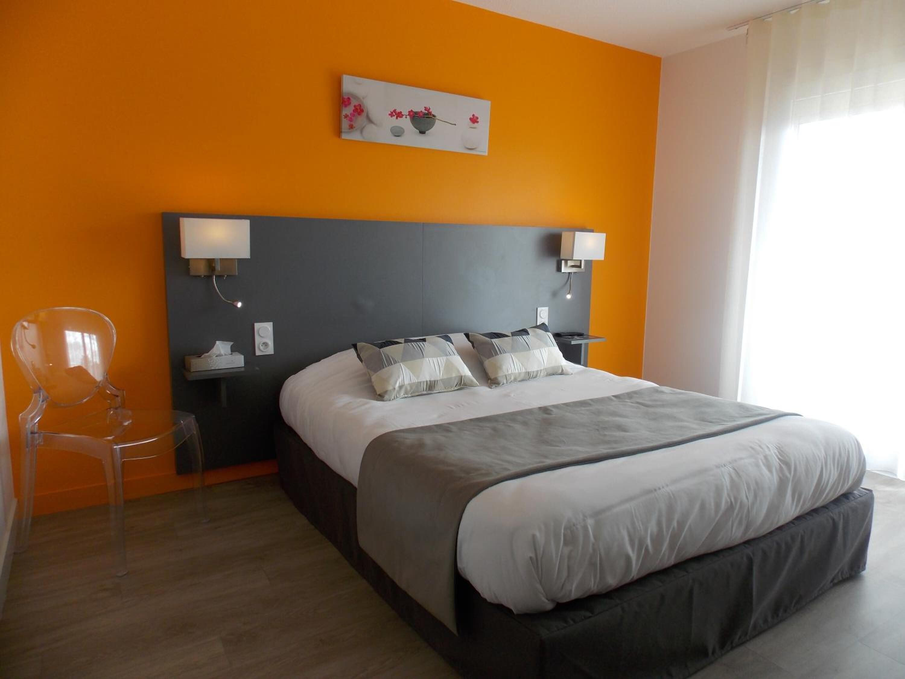 Een moderne hotelkamer met een groot bed, twee nachtkastjes met lampen, een transparante stoel en een schilderij aan de muur.