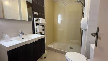 Uma casa de banho moderna com cabine de duche em vidro, uma sanita e lavatório branco.