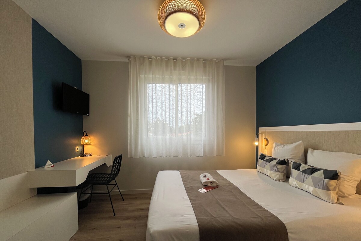 A hotel room with a bed, a desk, a chair, a television, and a window with curtains.