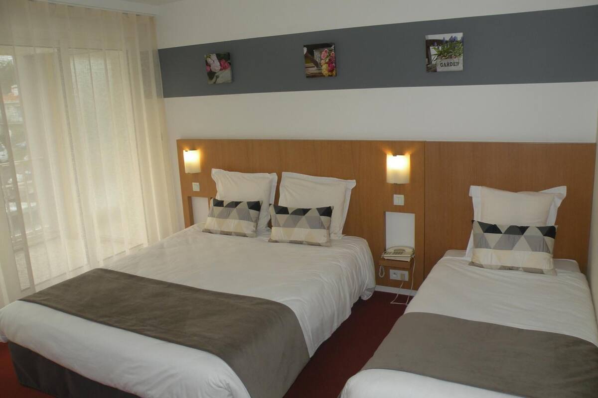 A hotel room with two beds, a wooden headboard, bedside lamps, and a window with sheer curtains.