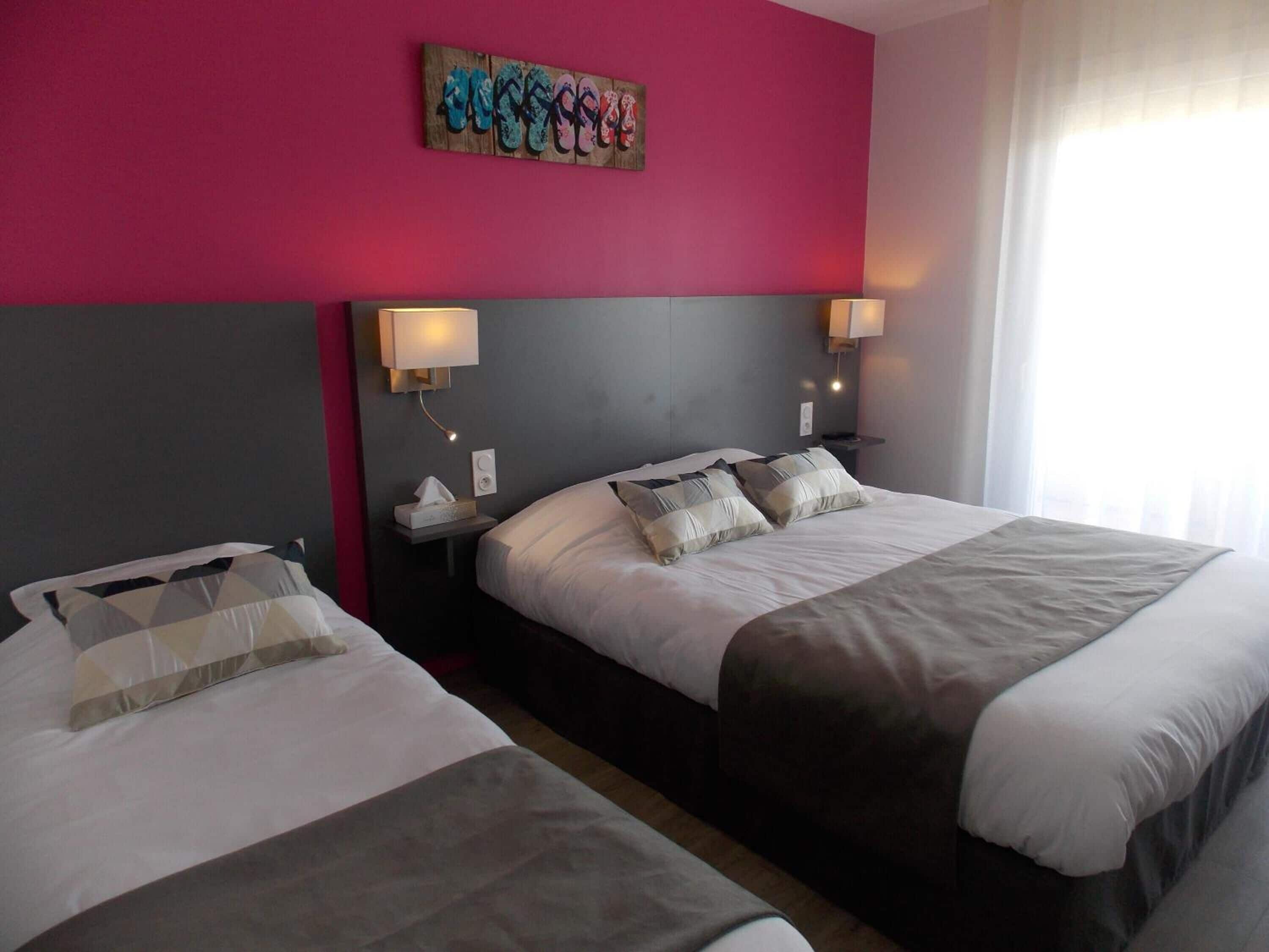 A hotel room with two beds, a pink accent wall, and a painting above the beds.