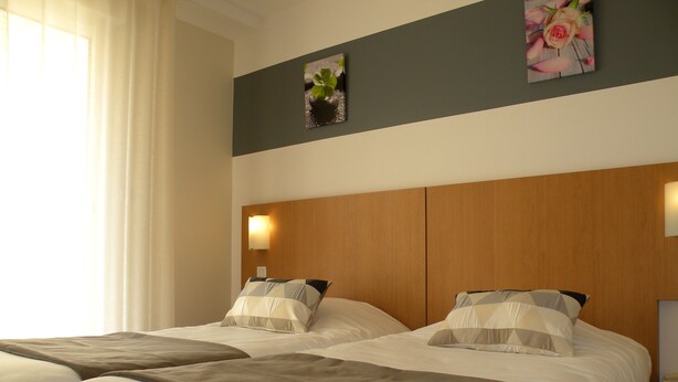 Een hotelkamer met twee bedden, een houten hoofdeinde en een kleine tafel met een lamp.