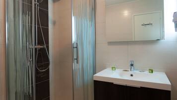 Een moderne badkamer met een douchecabine van glas, een wit wastafelmeubel en een spiegel erboven.